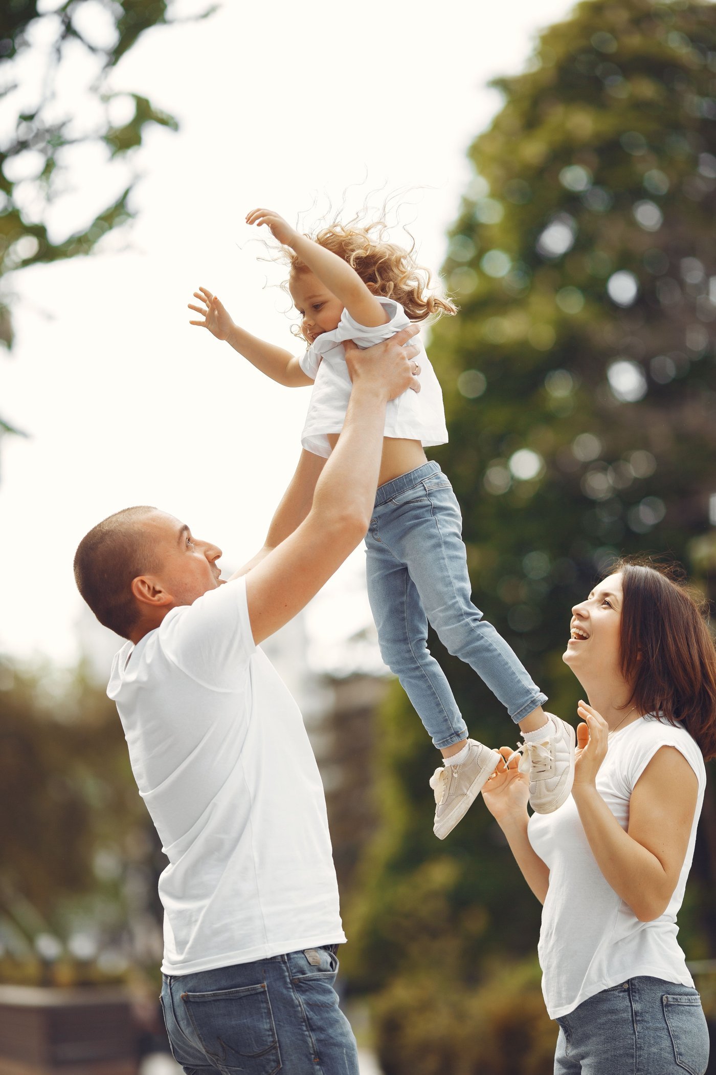 Father lifting daughter in the air while mother watches, smiling